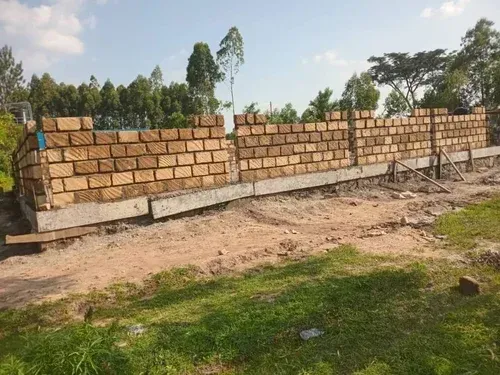Brick wall under construction, partially built on a concrete foundation, outdoors.