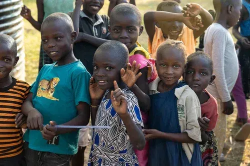 Children in Africa smiling, looking at the camera. Some are gesturing.