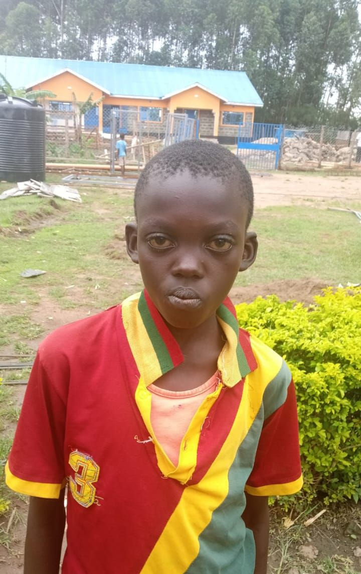 Young child with short hair wearing a blue and purple shirt, outdoors, looking somber.