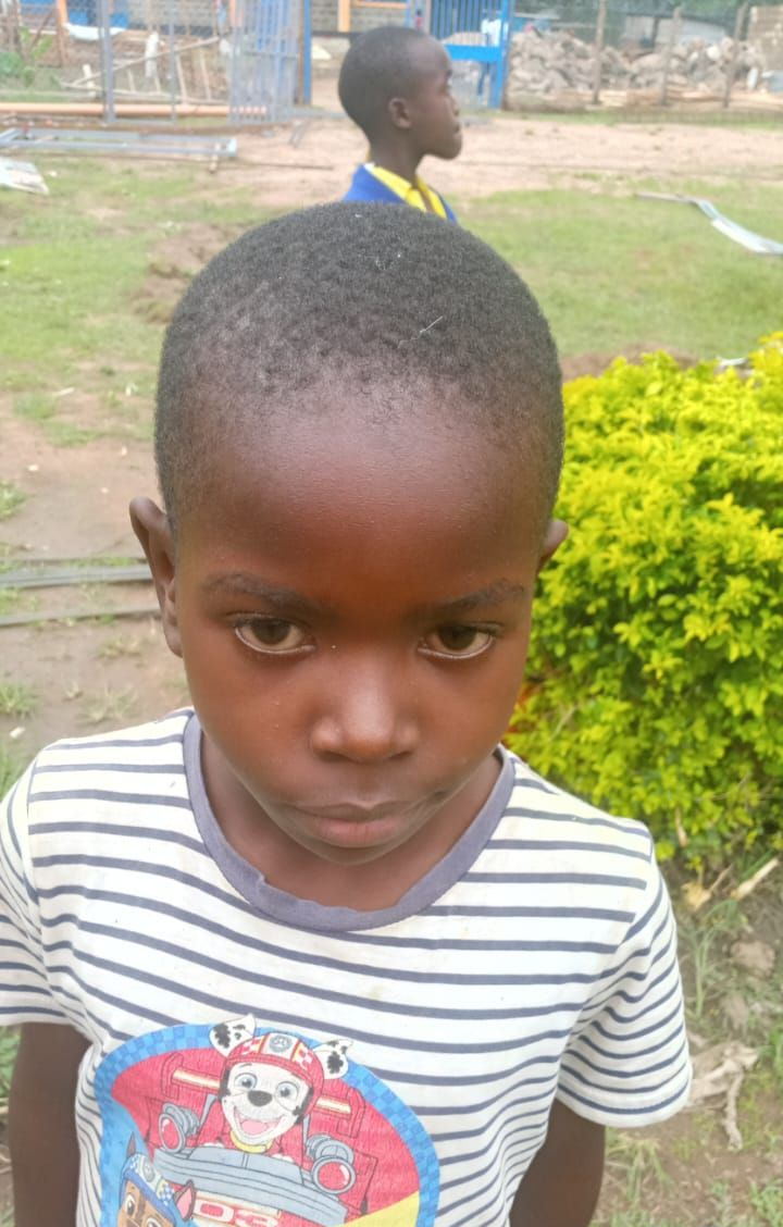 Young Black man in white shirt, looking at camera, in room with beds.
