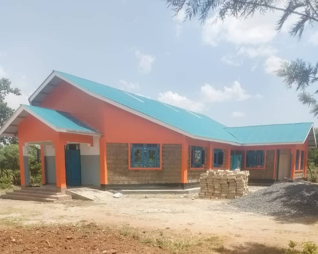 Construction of a single-story building. Stone walls are in progress, set amidst trees and greenery.