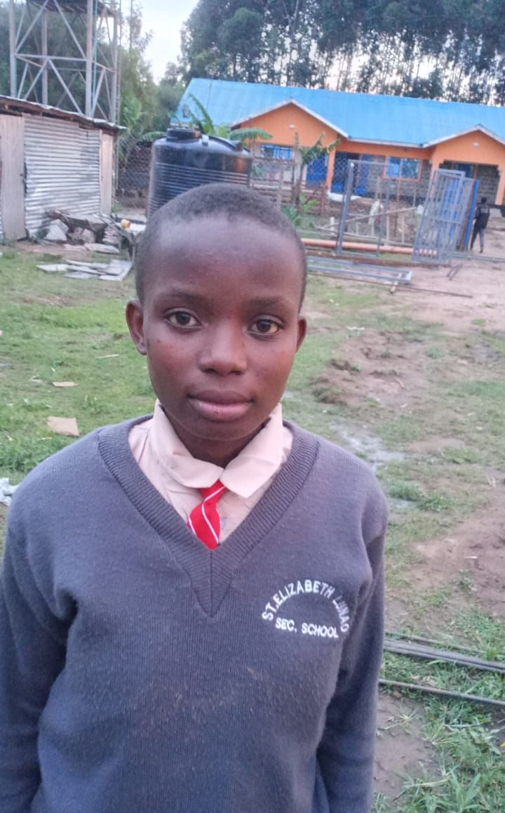 Young child with shaved head, wearing patterned blue and floral top, looking directly at the camera, outdoors.