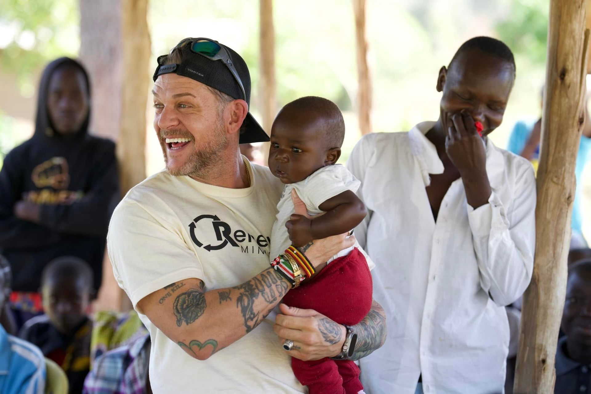Man holding baby, smiling, with others in a setting that appears to be outdoors.
