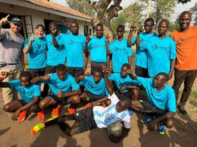 Group of people, mostly young men in turquoise shirts, posing with a soccer ball outdoors.
