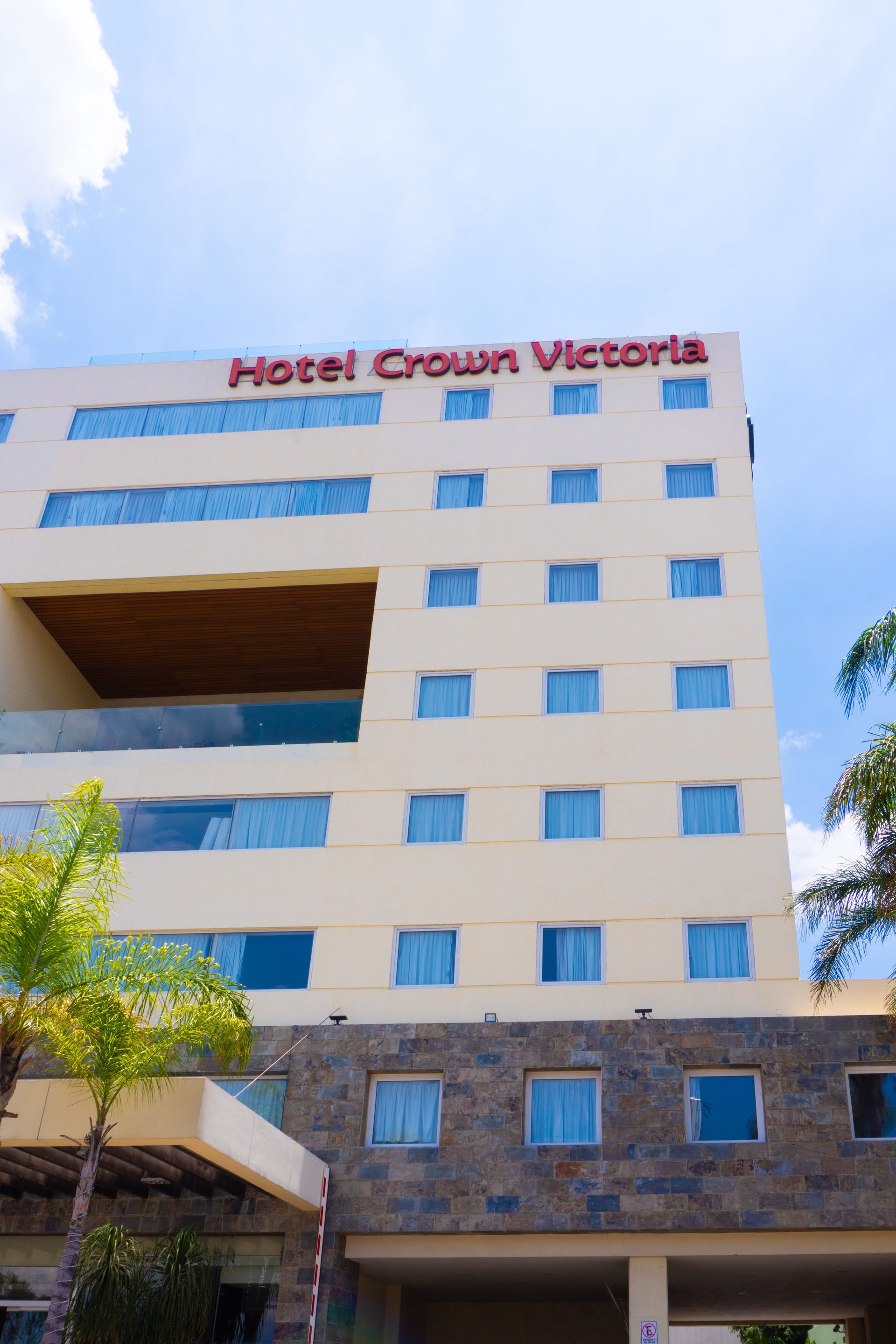 Exterior del hotel Crown Victoria con palmeras bajo un cielo azul.