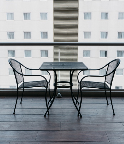 Mesa y sillas de metal negro en un balcón con un edificio de la ciudad al fondo.