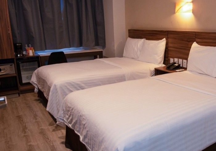 Una habitación de hotel con dos camas, un escritorio, una mininevera y un cabecero de madera.