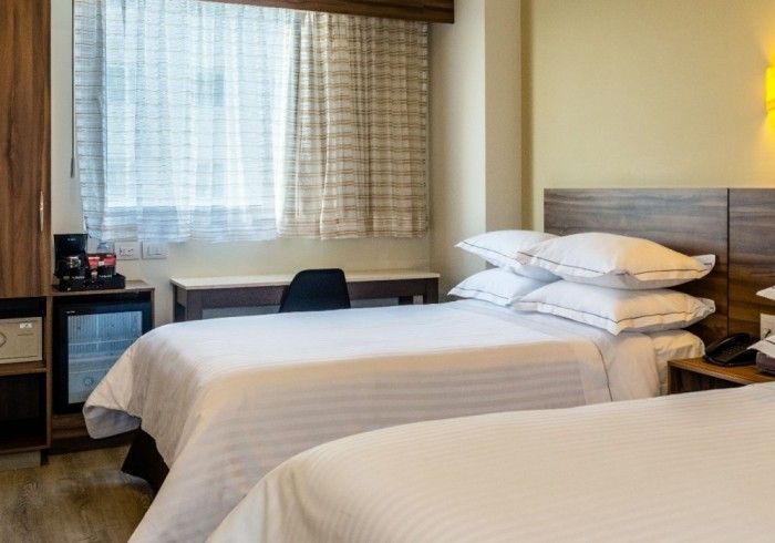 Habitación de hotel con dos camas, escritorio junto a la ventana y minibar.
