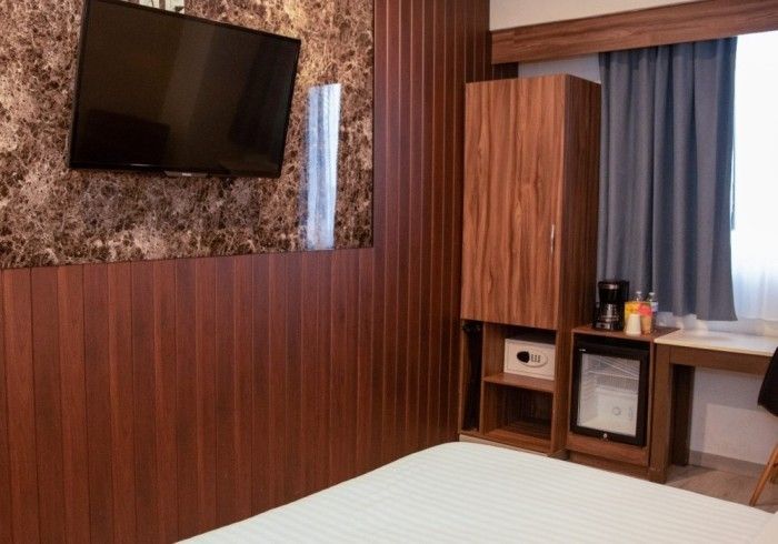 Habitación de hotel con televisor de pared, paneles de madera y una pequeña nevera.