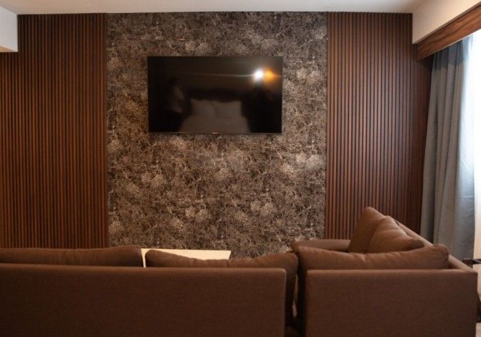 Salón marrón con televisor de pared, sofá marrón y pared decorativa con textura.