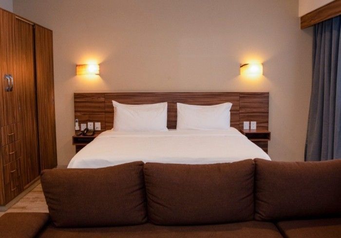 Dormitorio con cama, mesitas de noche, apliques de pared y sofá frente a la cama. Tonos marrones y blancos.