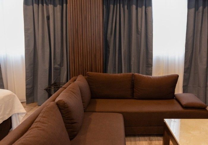 Sofá seccional marrón en una habitación con cortinas grises y paneles de madera.