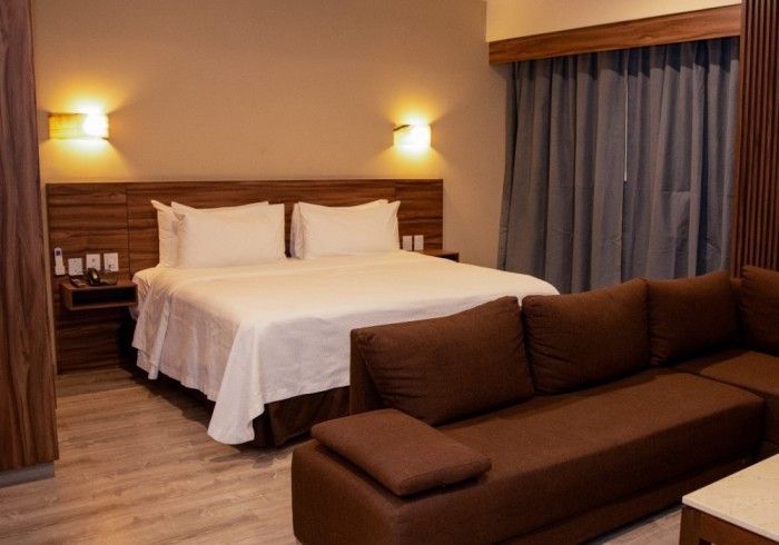 Habitación de hotel con cama, sofá y mesitas de noche. Combinación de colores marrón y crema.