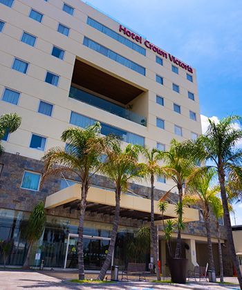 Exterior del hotel Crown Victoria con palmeras bajo un cielo azul.