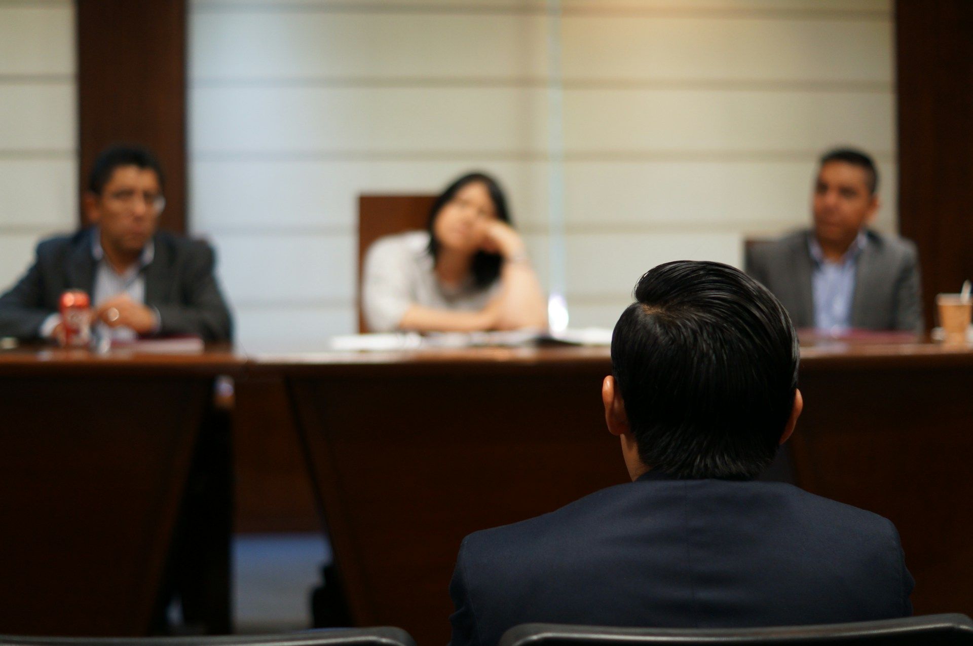 Conference panel hearing with three seated speakers facing an audience member in the foreground.