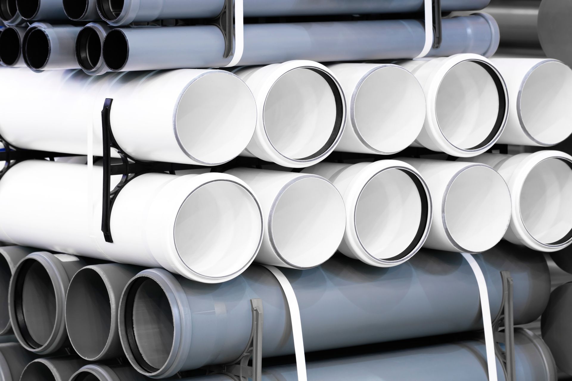 Stack of gray and white plastic pipes on shelves, for construction or plumbing.