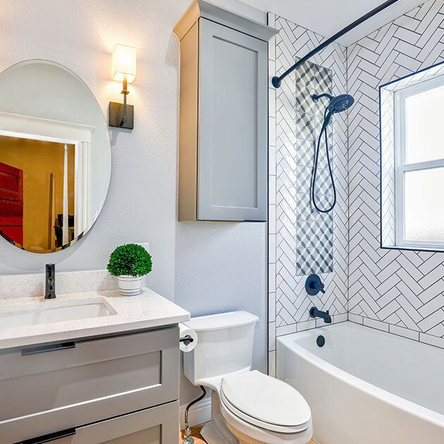 Bathroom with gray vanity, oval mirror, and white herringbone tile in shower.