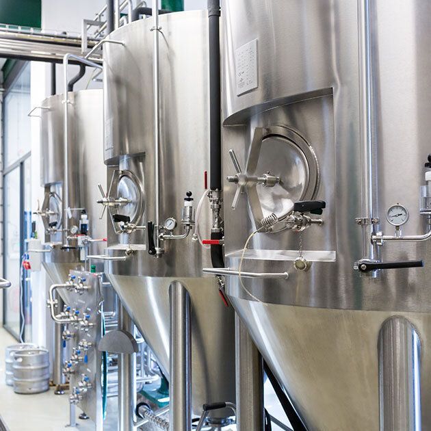 Stainless steel brewing tanks in a brewery, with valves, gauges, and a keg.