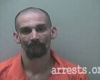 A man with a beard and bald head is wearing an orange prison uniform.