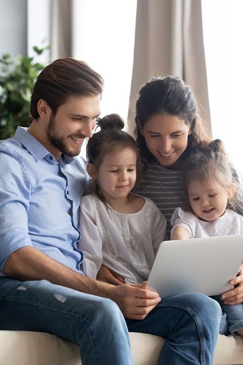 A family is sitting on a couch looking at a laptop computer.