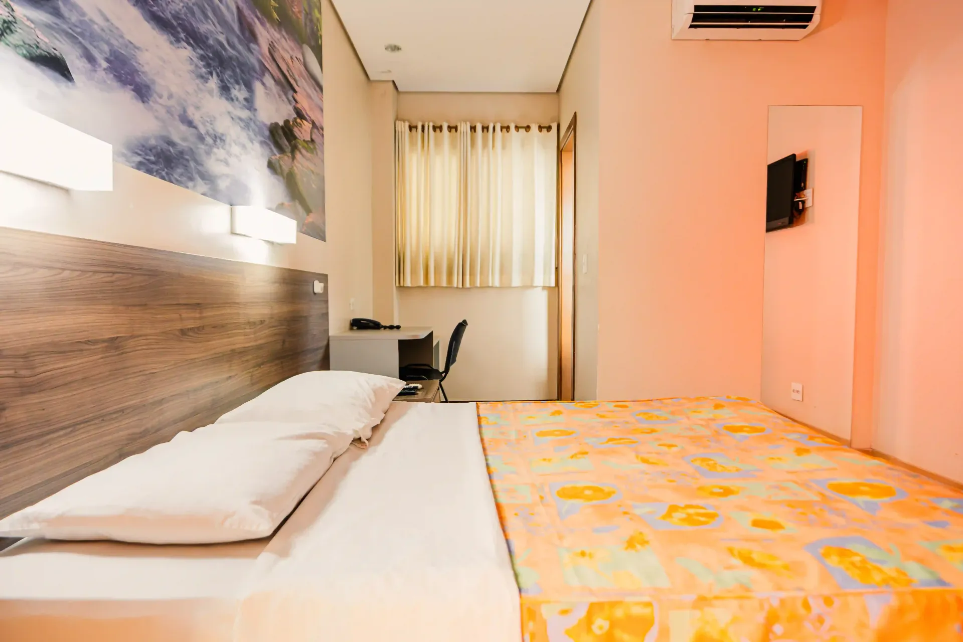 Um quarto de hotel com duas camas, uma escrivaninha e uma televisão.