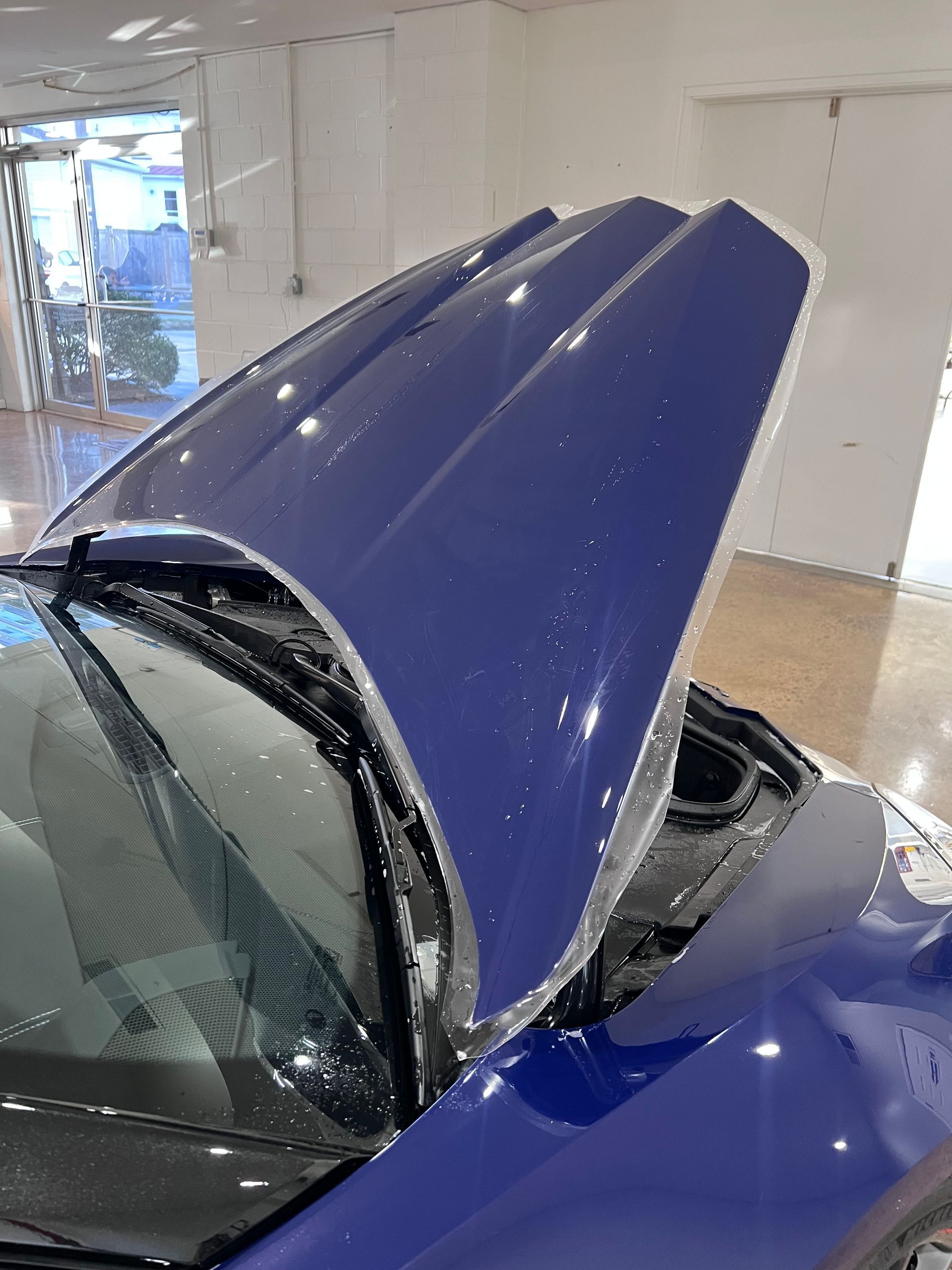 A blue car with the hood open is sitting in a room.
