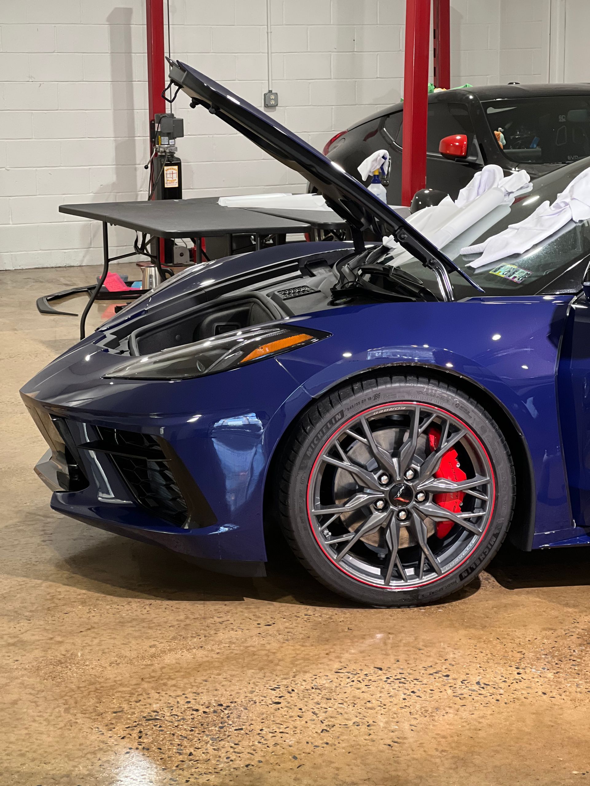 A blue sports car with the hood up is parked in a garage.
