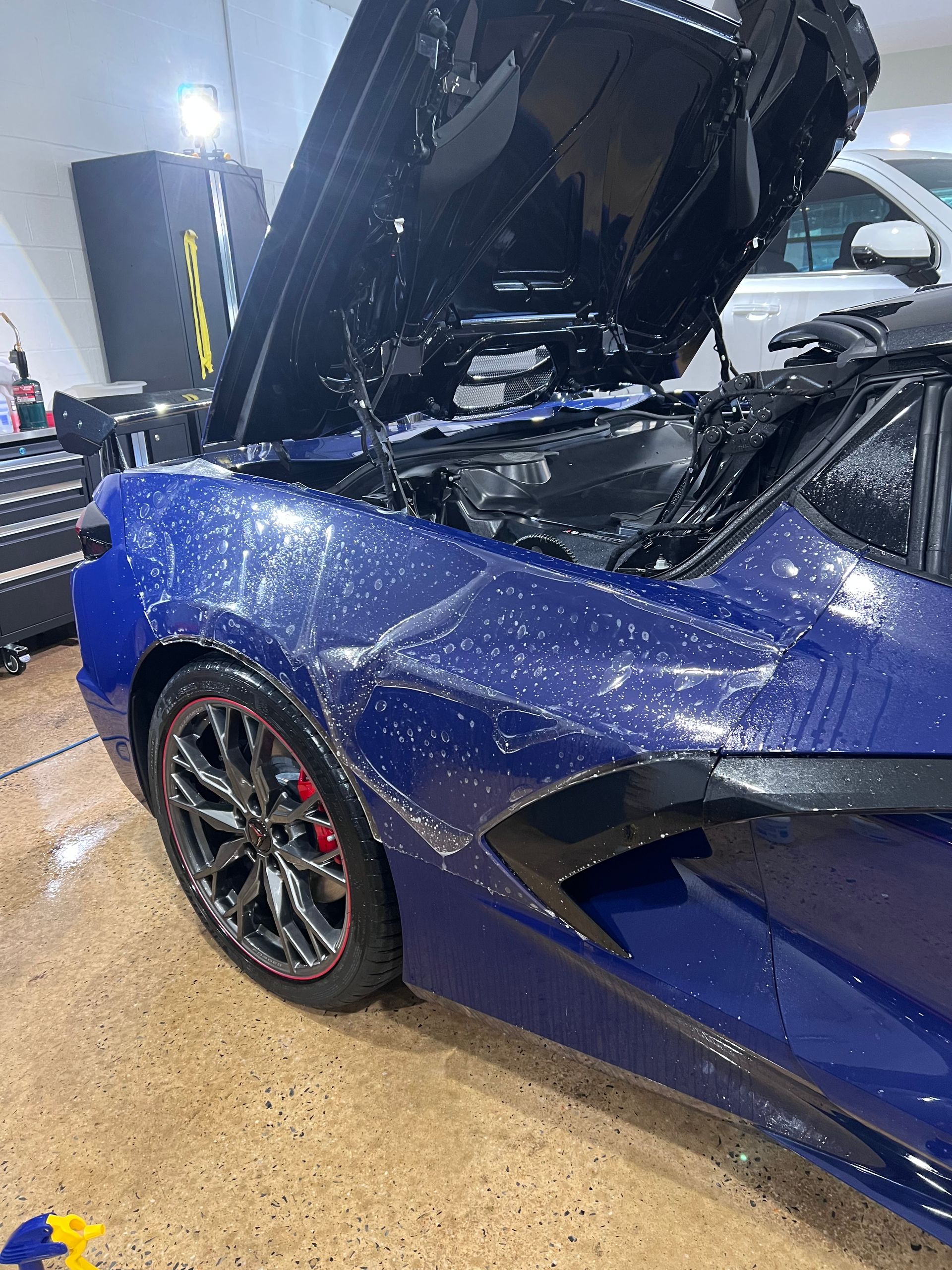 A blue sports car with the hood up is parked in a garage.