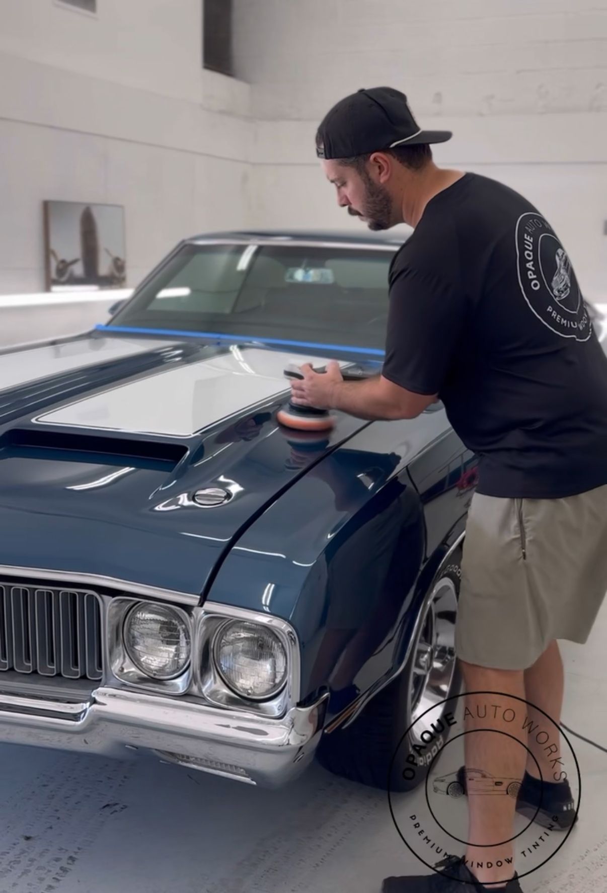 A man is polishing the hood of a blue car