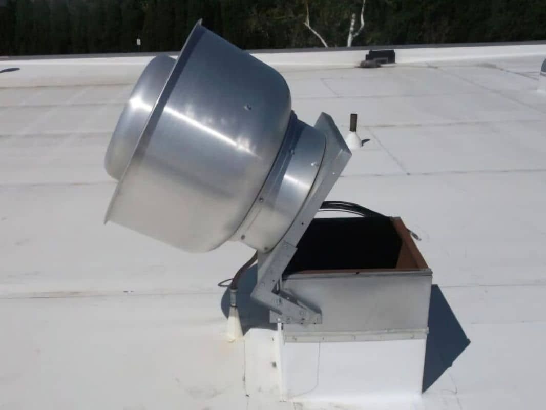 A white roof with a hinged metal exhaust fan on it tilted open.