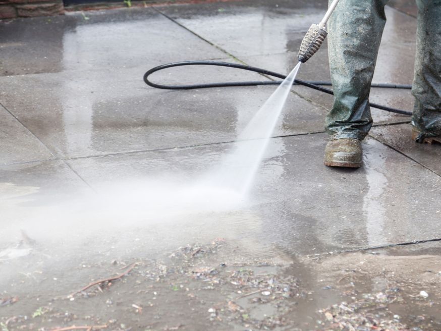 A man is using a high pressure washer to clean a concrete floor.