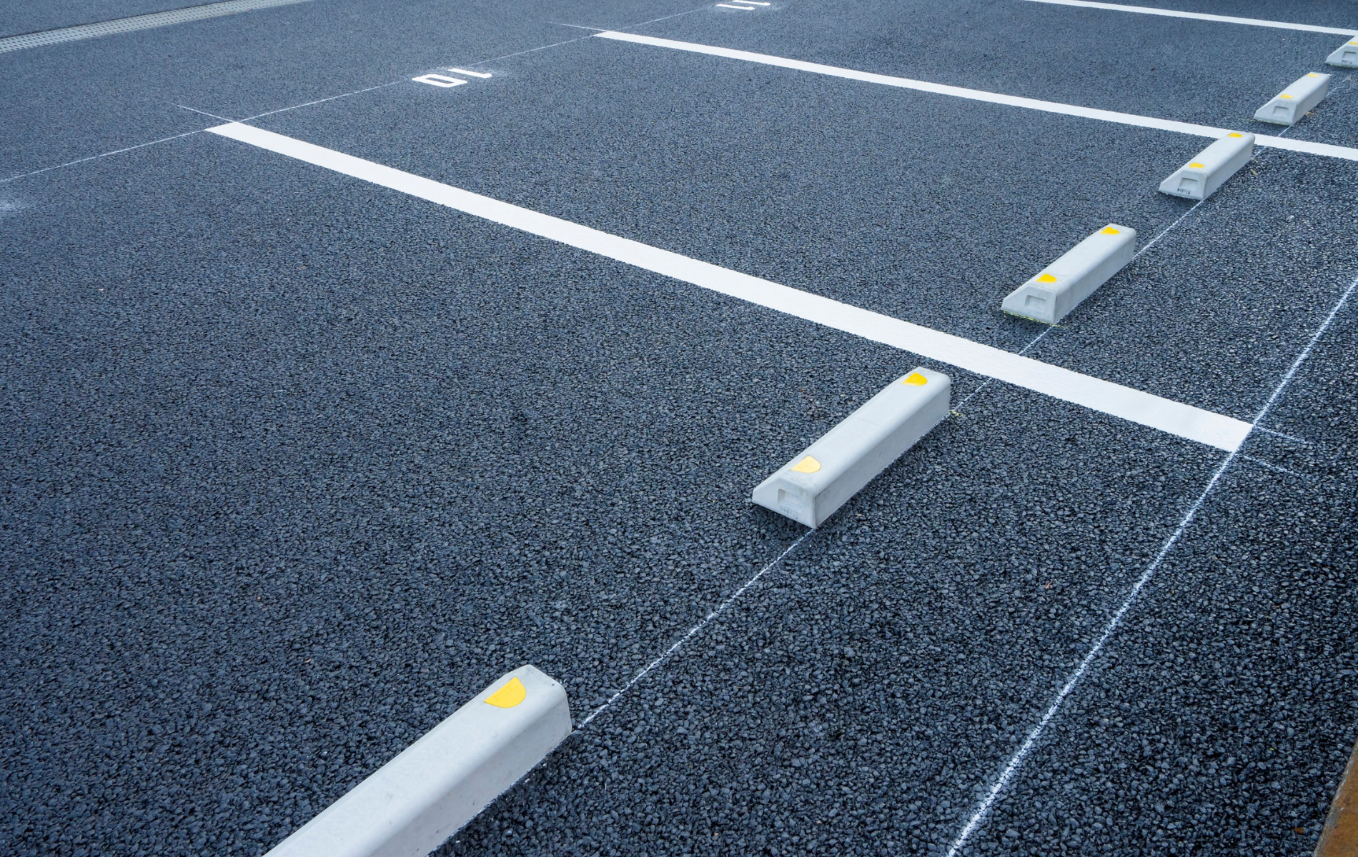 Parking lot with asphalt surface, white lines, and concrete parking blocks.