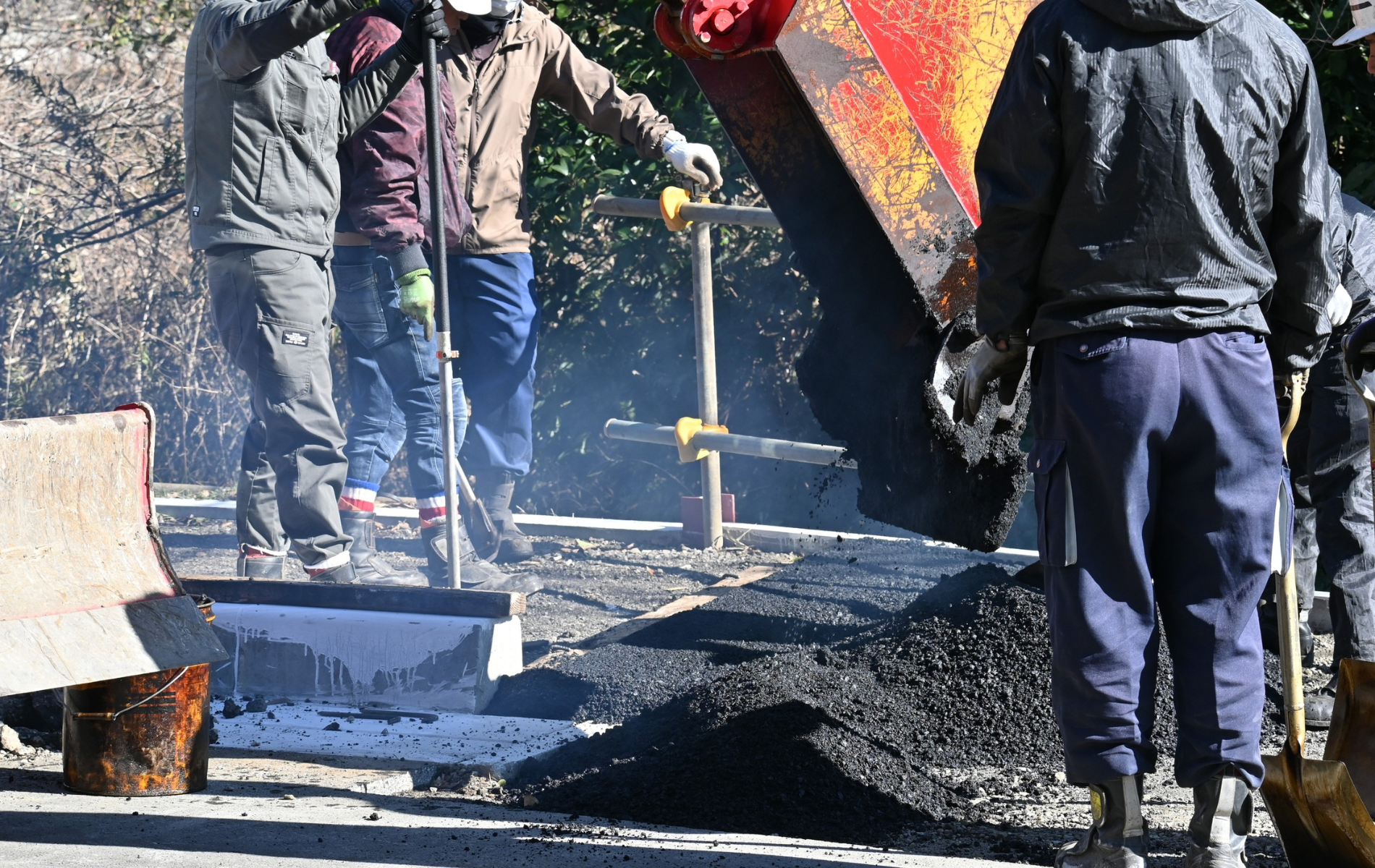 Road workers pouring asphalt from a truck onto a road surface.