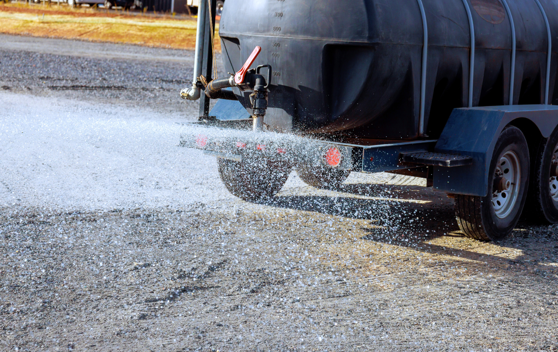 Black tank trailer spraying water on gravel.