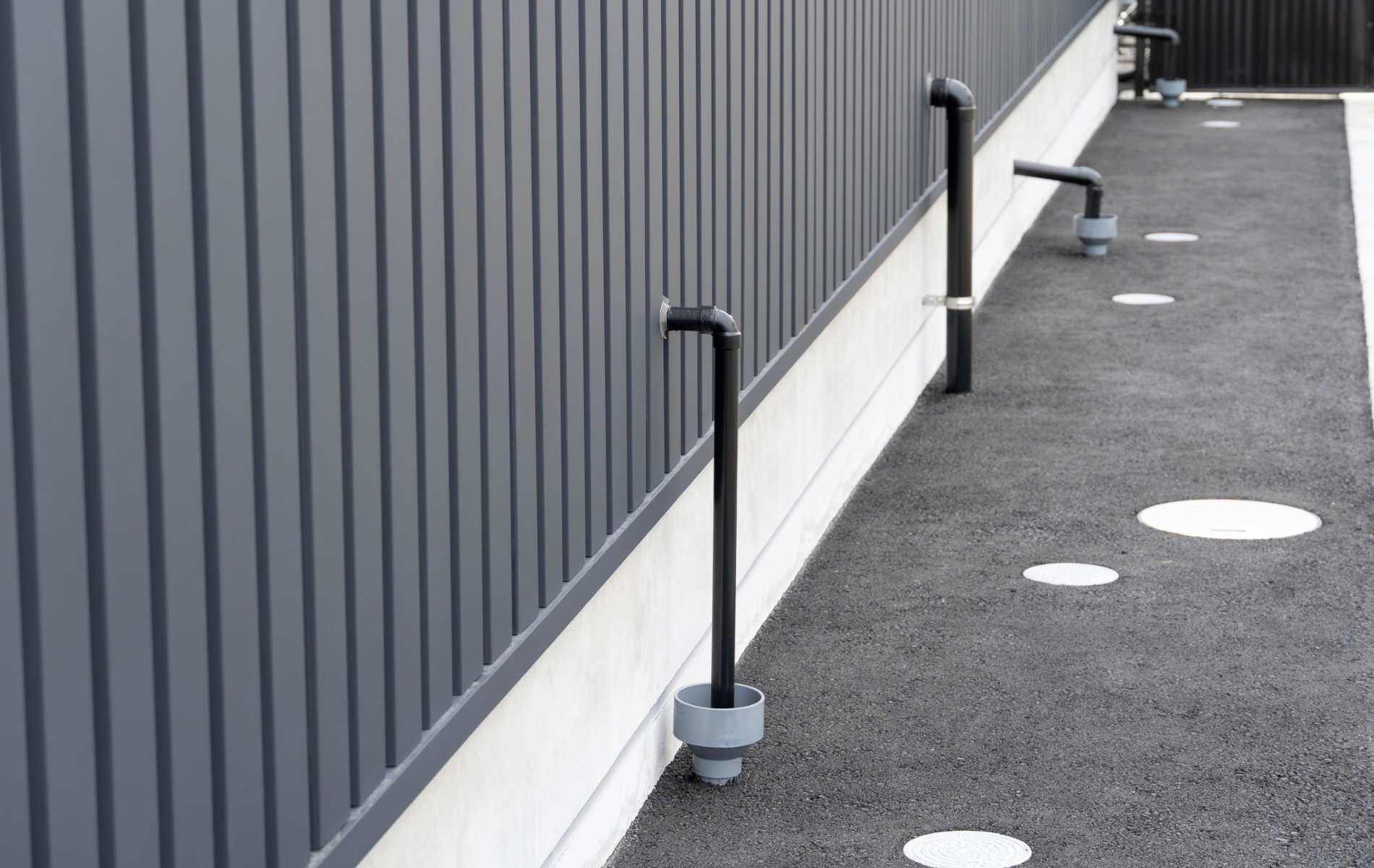 Gray metal wall and walkway with black pipes and white circular covers.