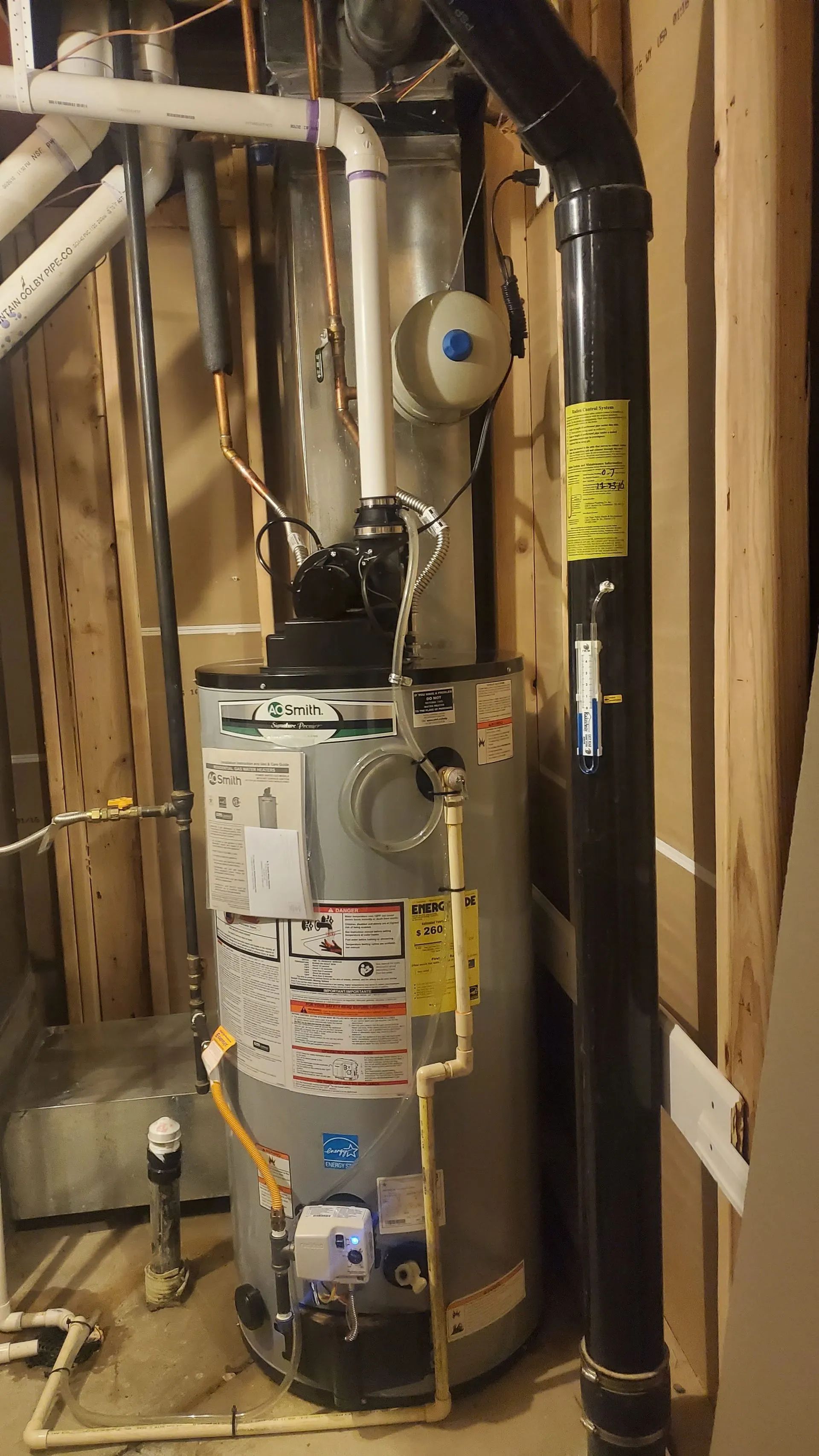 Water heater in a utility closet with exposed pipes and ductwork, showing a gas vent and control panel.