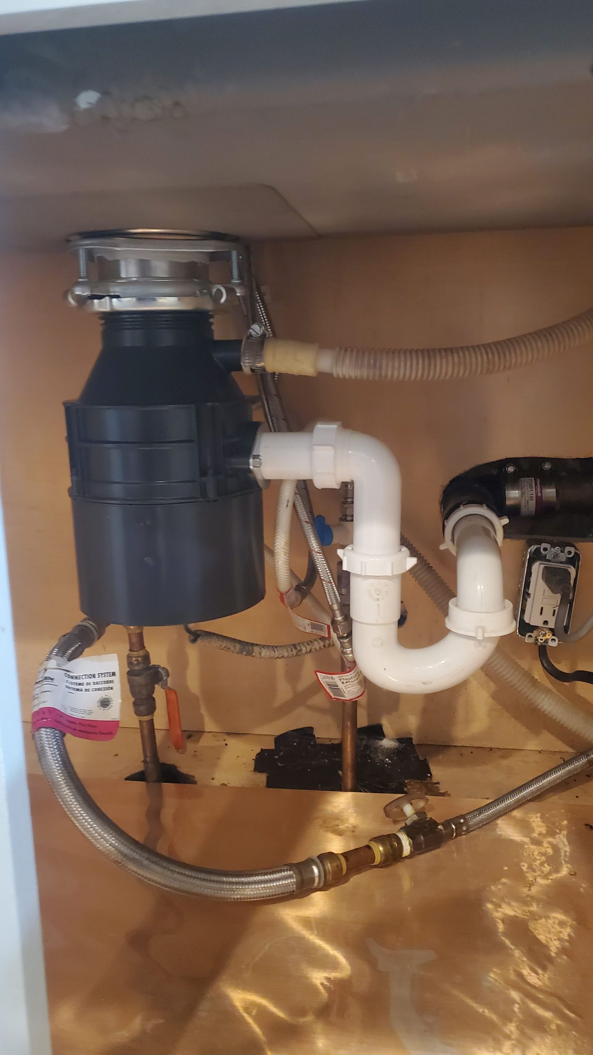 Garbage disposal unit under a kitchen sink with connected plumbing.