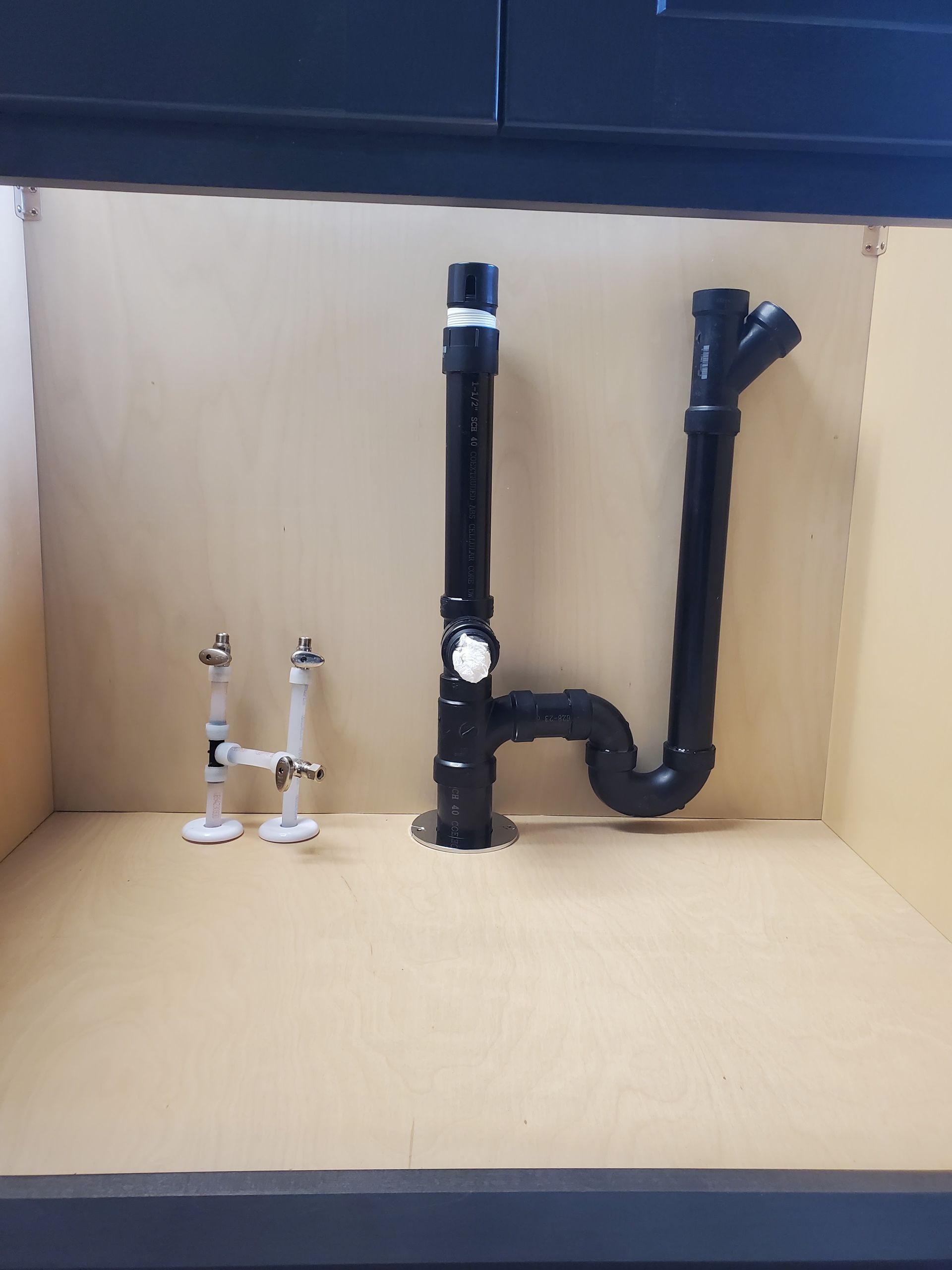 Plumbing fixtures inside a cabinet: drain pipes and shut-off valves in a kitchen.
