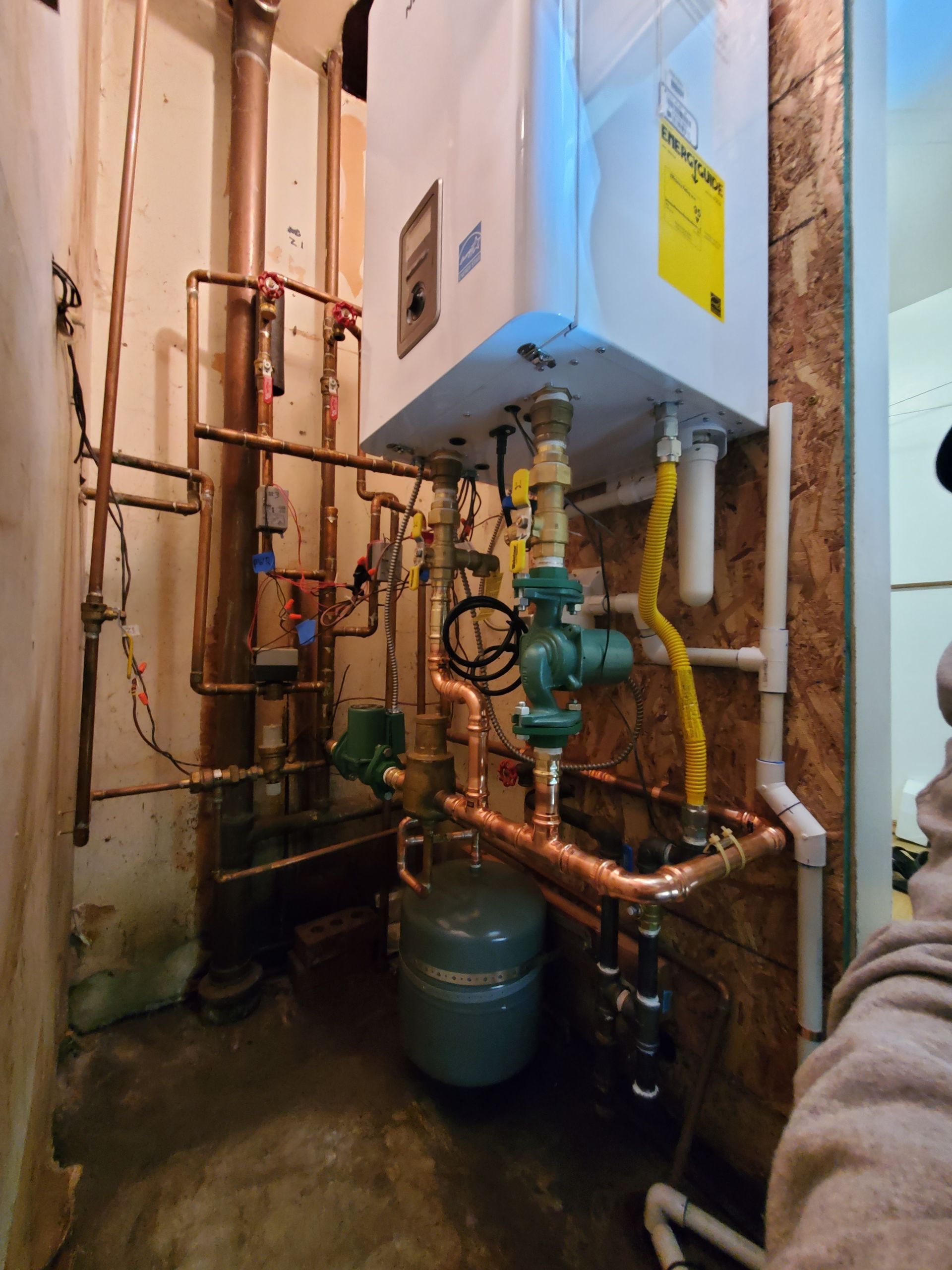 Copper pipes and a boiler in a utility room. Blue and white equipment is attached to the wall.