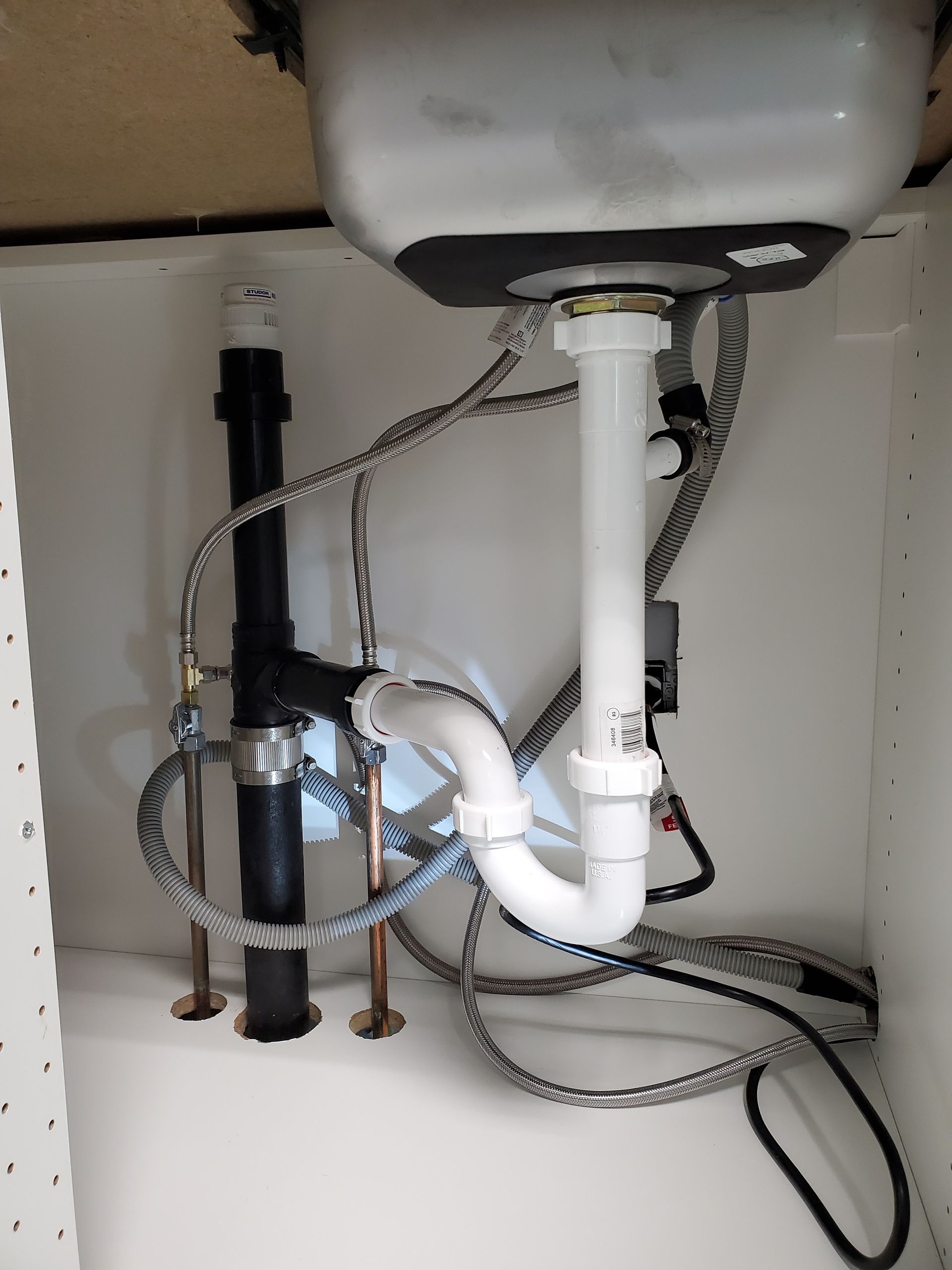 Under-sink plumbing with a black drainpipe, white P-trap, and silver braided supply lines.