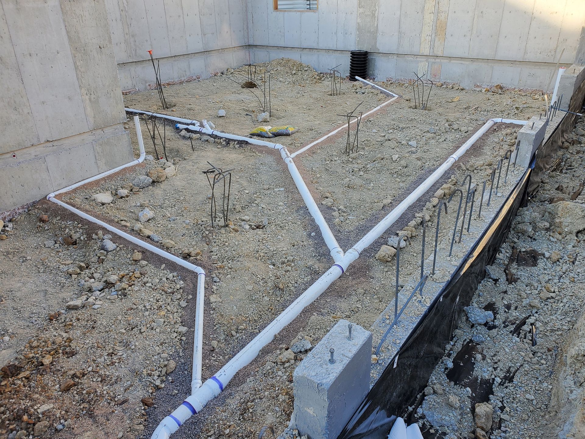 Interior view of a foundation with gravel, pipes, and rebar for drainage.