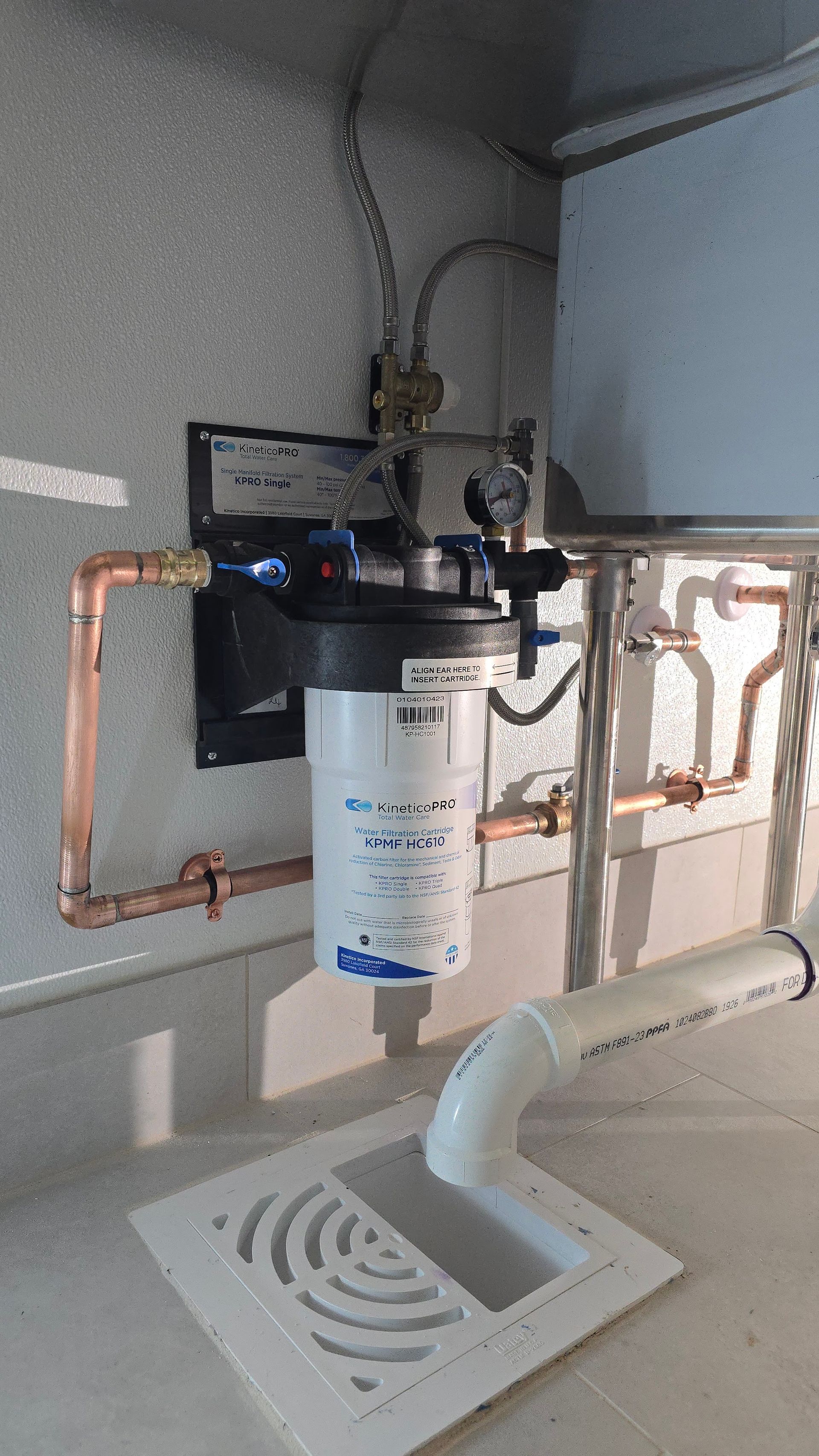 Water filtration system with copper pipes, drain, and wall-mounted components against a concrete wall.
