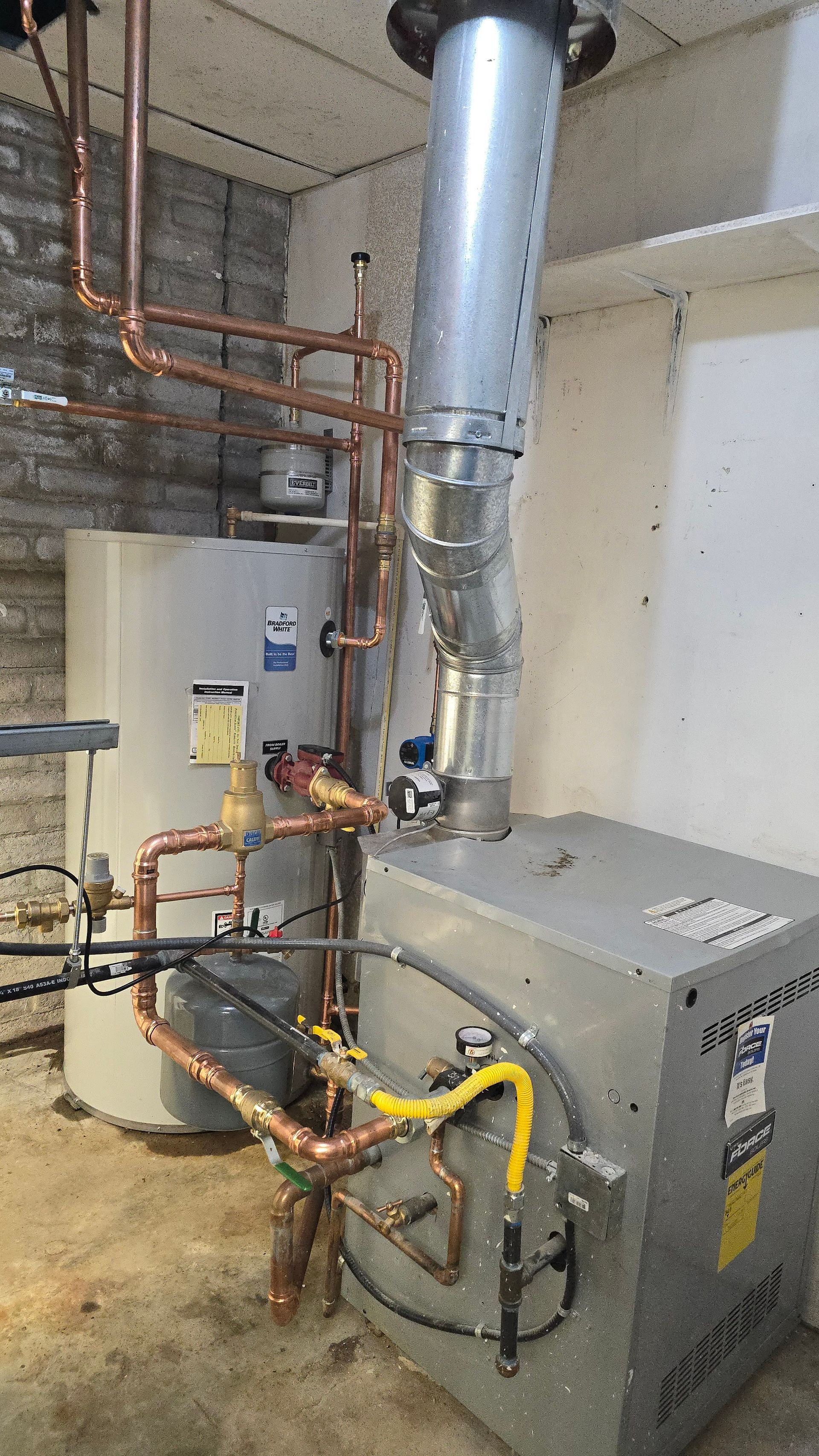 A boiler system with copper pipes, a water heater, and a metal flue in a basement.