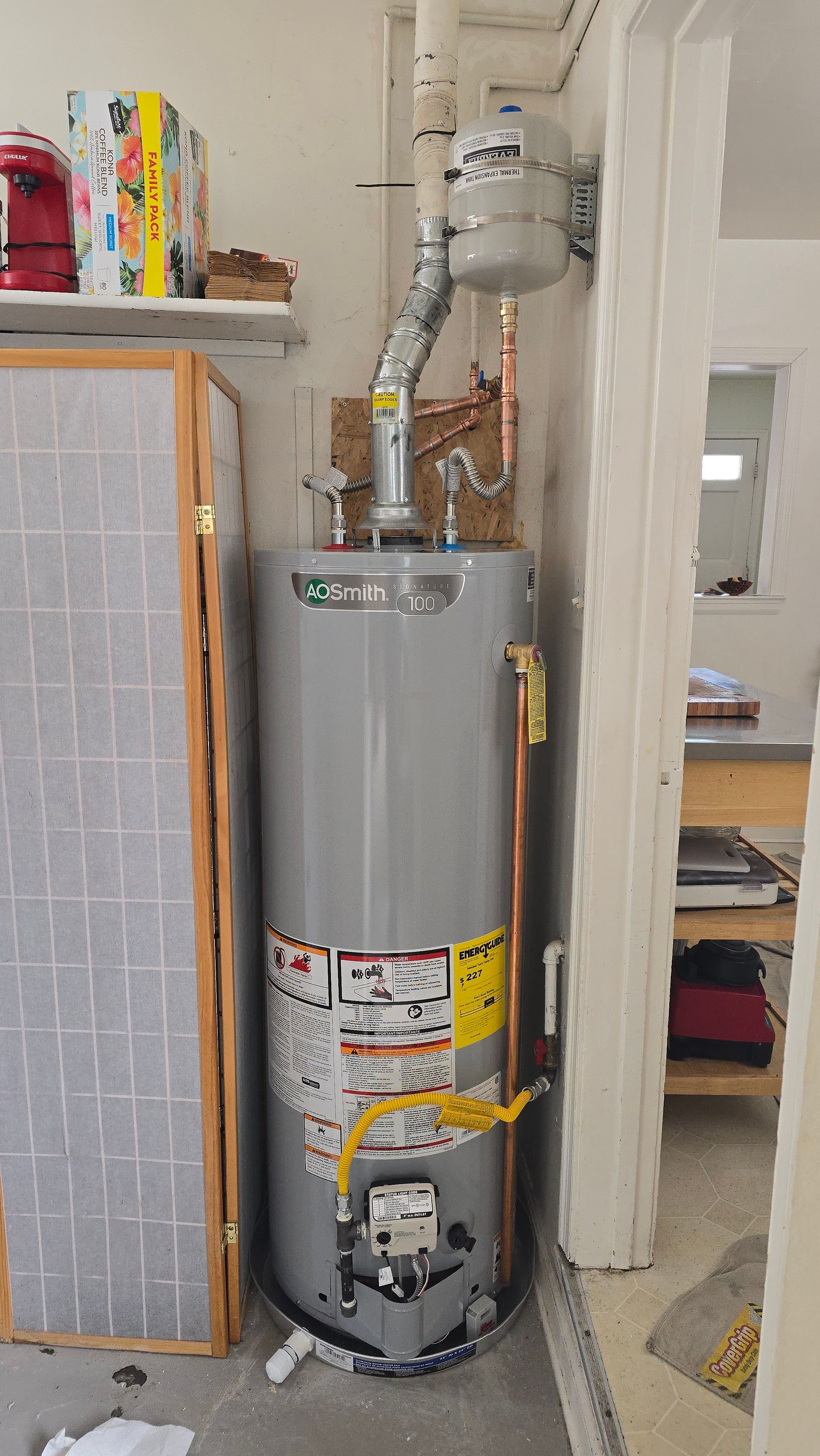A tall, gray water heater with yellow energy label is installed in a garage.