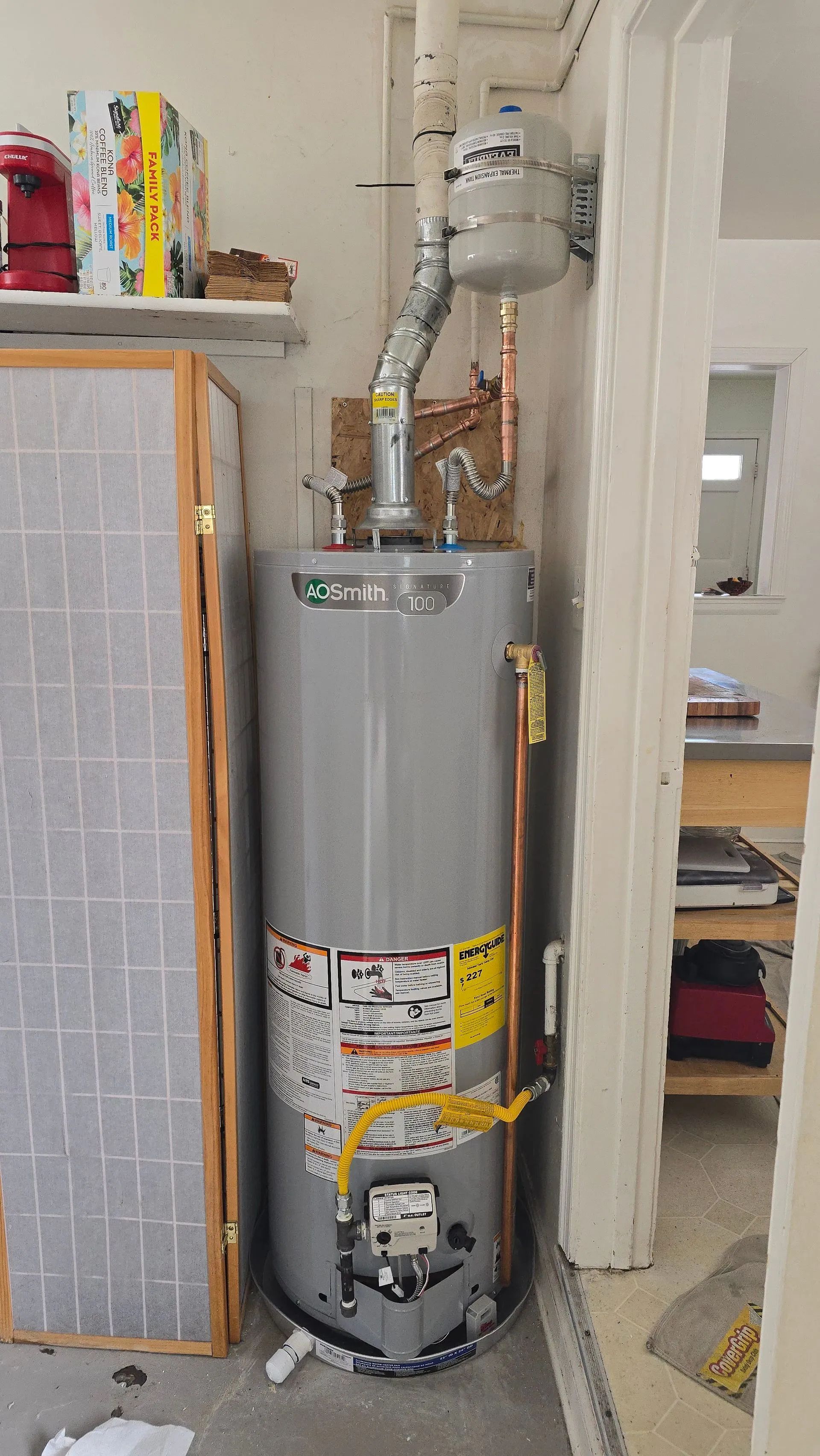Water heater in a narrow utility closet with pipes and a vent pipe above it