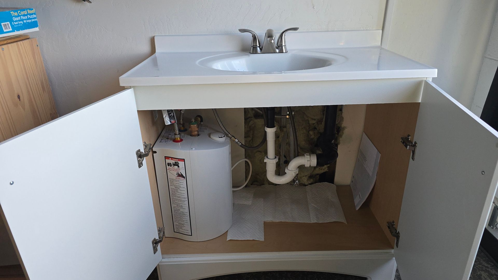 White bathroom vanity with open doors, small water heater inside.