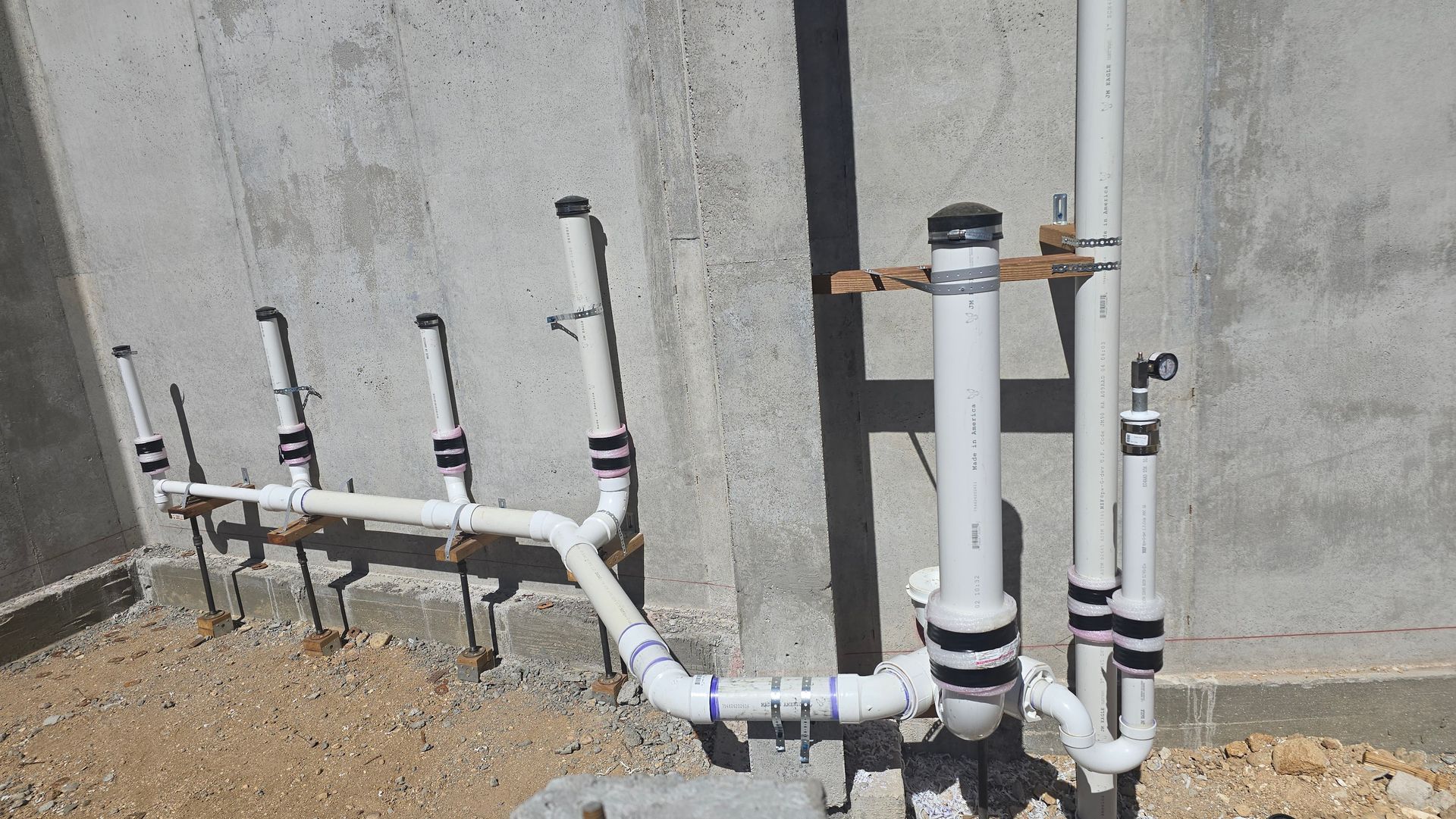 White PVC pipes with black fittings against a concrete wall, outdoors.