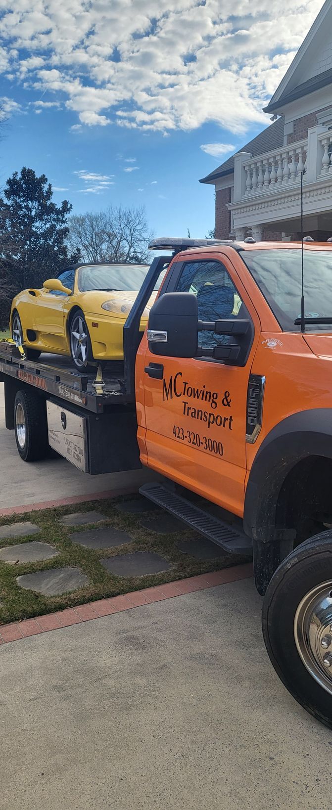 A yellow convertible sports car is being transported on the flatbed of an orange tow truck parked in front of a house.