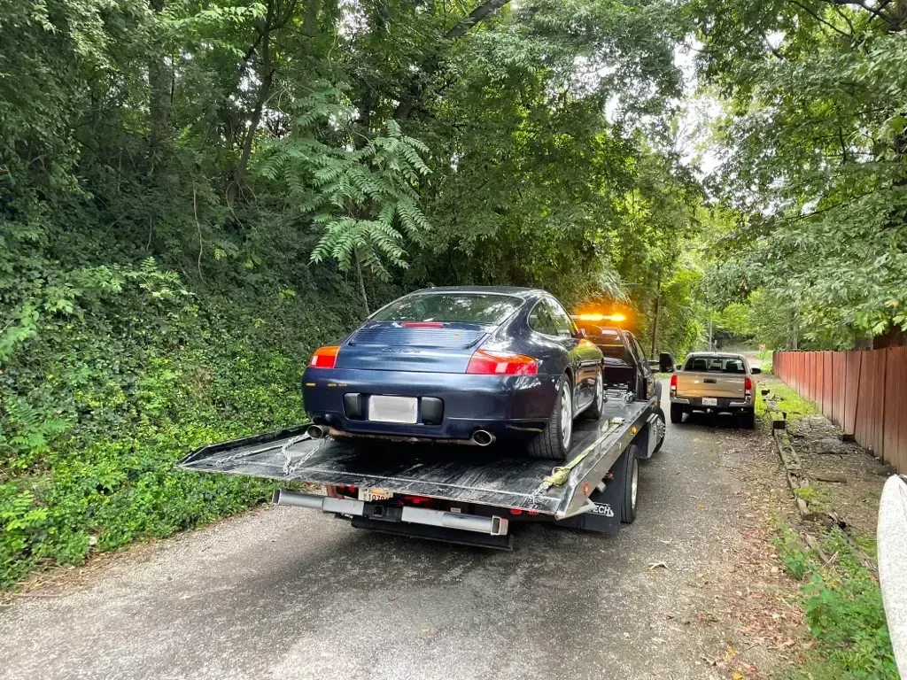 Tow truck towing a dark car on a residential street; bright sunny day.