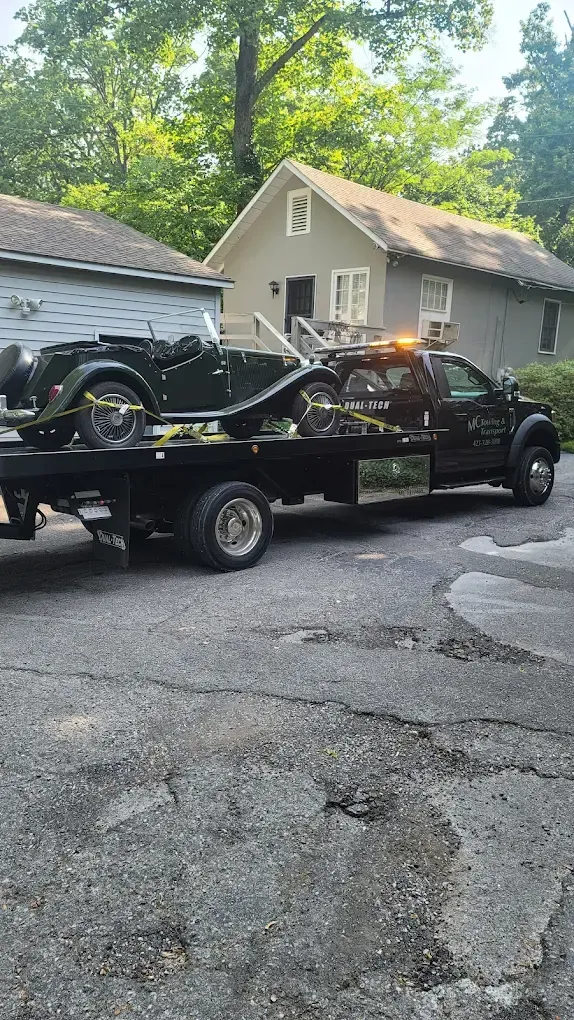 Black SUV being towed by a red tow truck on a sunny day.